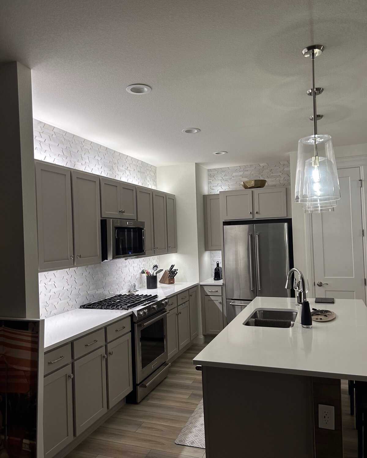 Modern kitchen remodel with under-cabinet lighting, recessed cans, and pendants